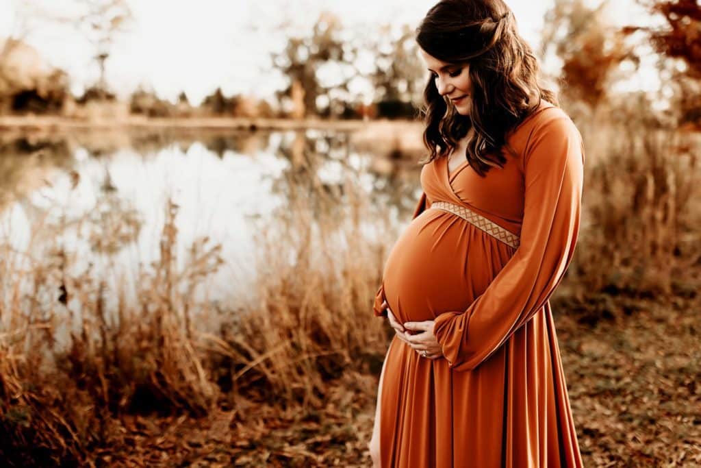 Warner Robins expecting mom in gorgeous orange maternity gown looking down at growing belly.