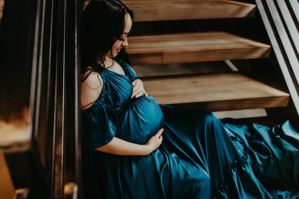 Expecting mother sitting on stairs while loving holding and gazing her baby bump