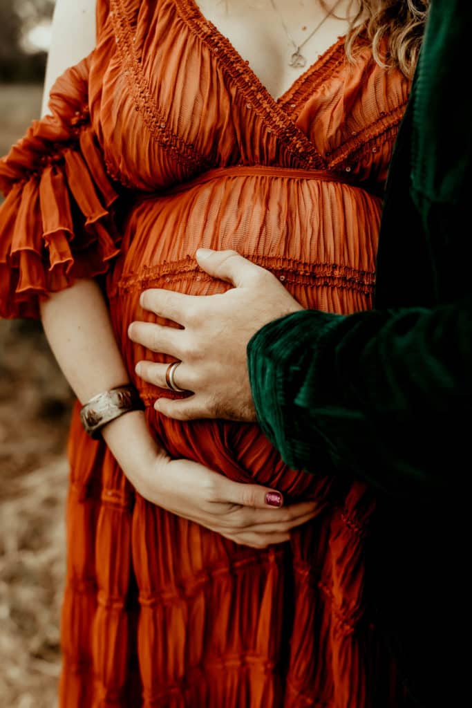 Hands on the baby bump of pregnant mom in a rust designer gown.