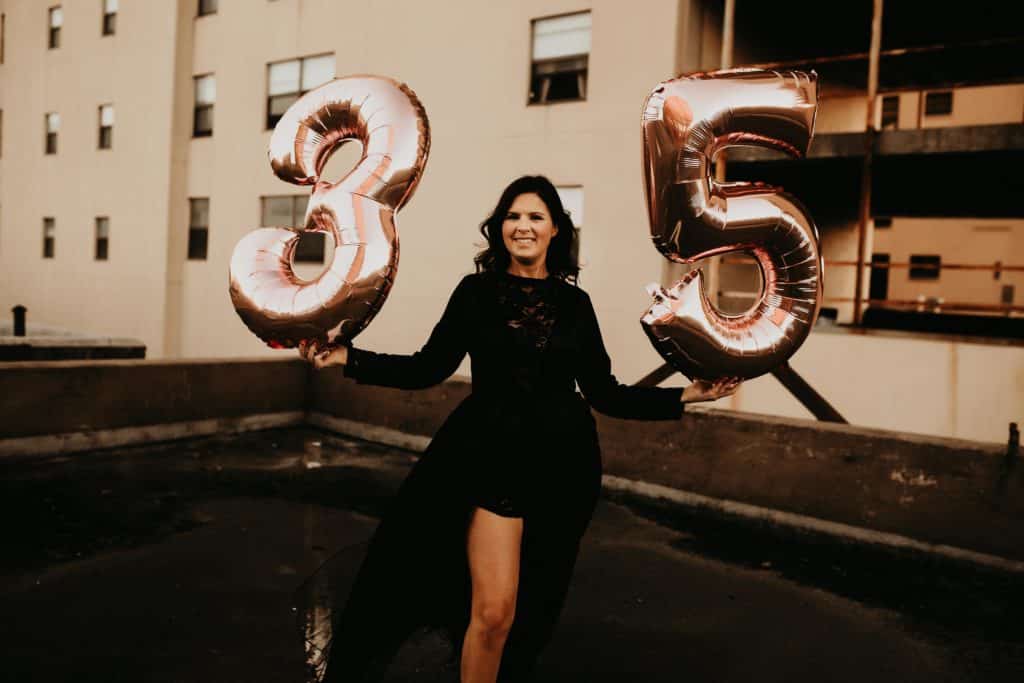 Woman holding pink number balloons for 35th birthday on a downtown urban rooftop. 