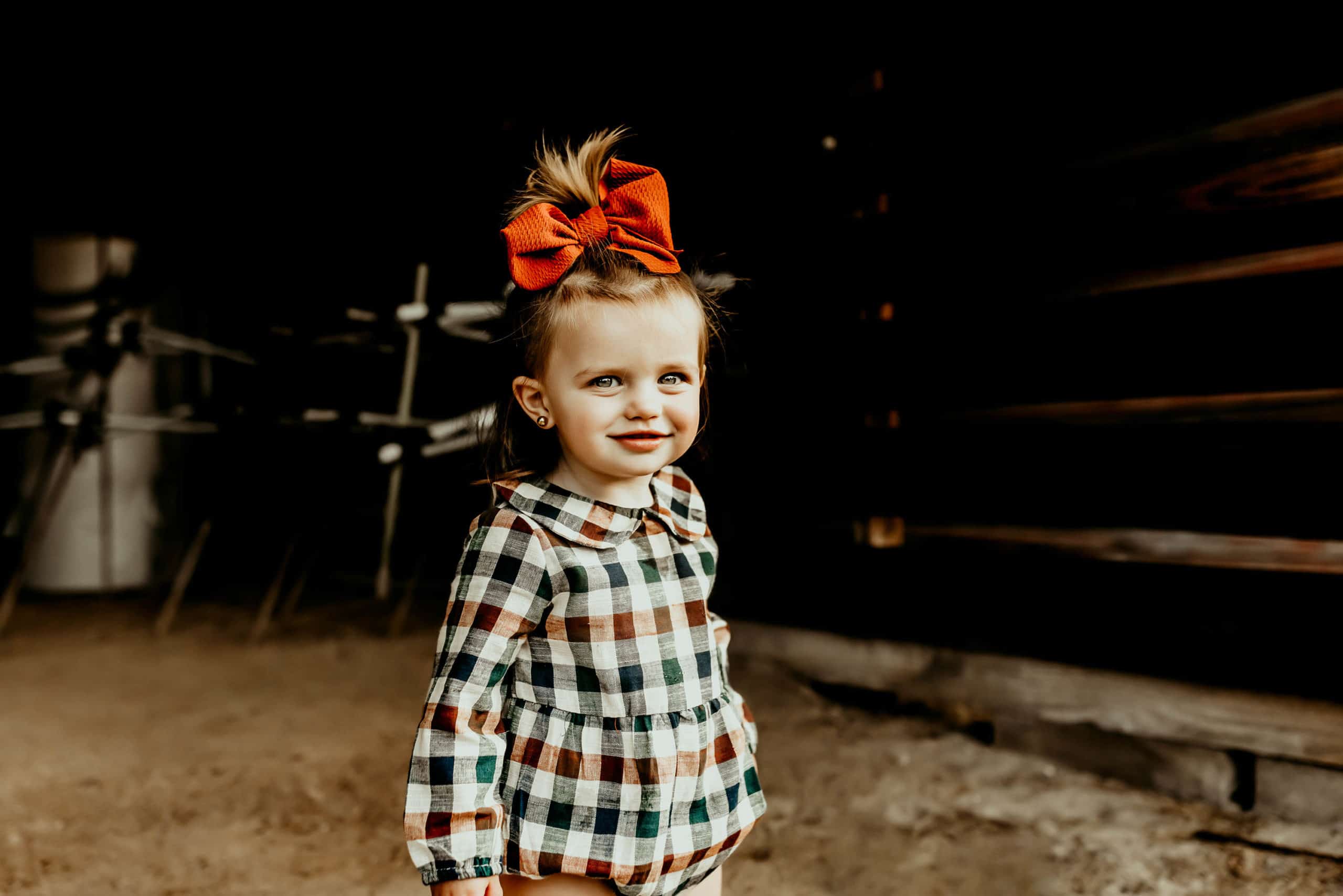 2 year old little girl in a blue and orange plaid romper with a big orange bow in her hair captured by Warner Robins photographer.