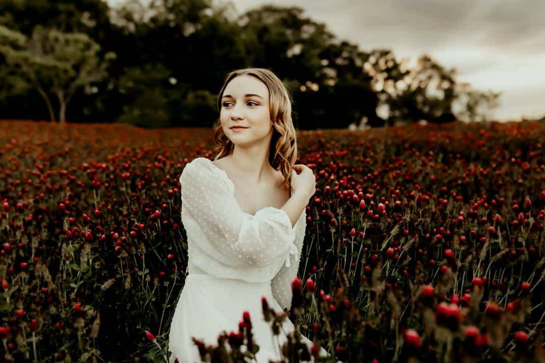 Teenage girl sitting in a red clover field looking off in the distance captured by Fire Family Photography