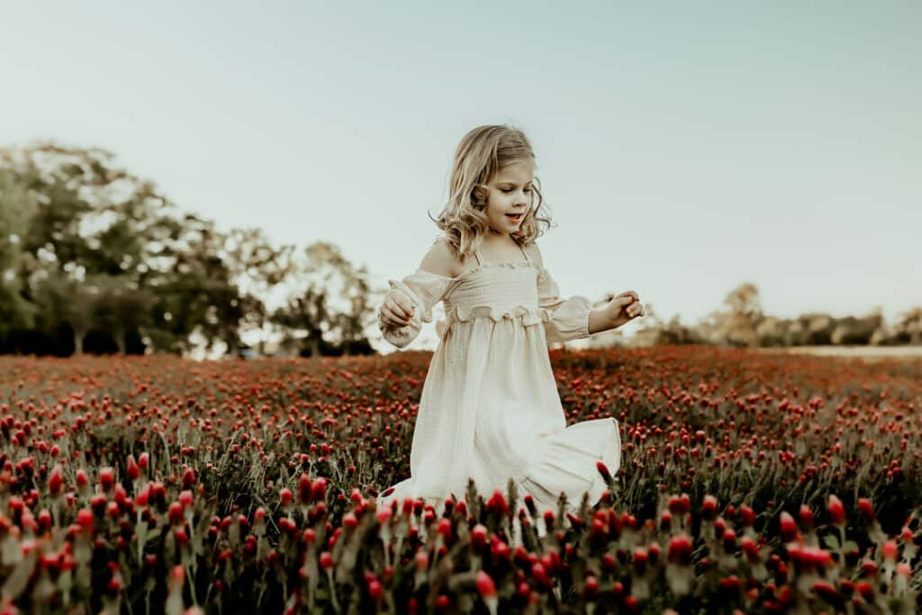 little girl walking in a field of red clovers 