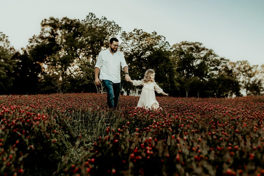 Father and daughter walking in a field of red clovers blooming in Perry GA captured by Fire Family Photography