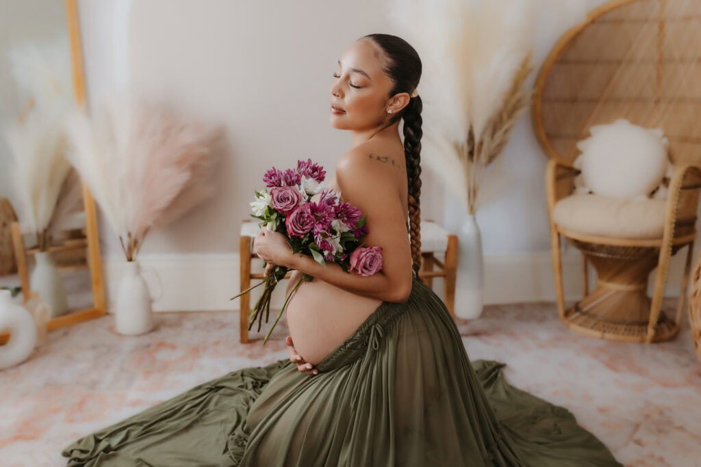 Maternity Session Prep Checklist: What to Wear, What to Bring, and How to Feel Ready 2 Pregnant woman holding a bouquet with bare belly and flowing green skirt in studio light