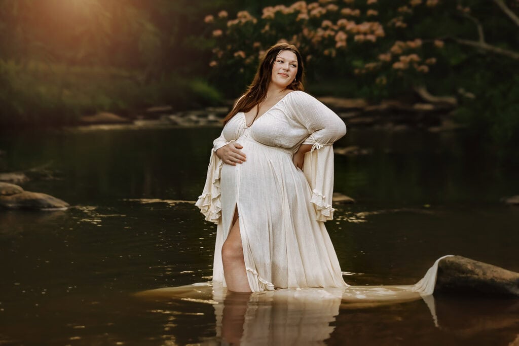Best Time to Schedule Maternity Photos (So You Actually Feel Like Yourself) 2 Outdoor maternity photo of an expecting mother standing in shallow water wearing a flowing dress