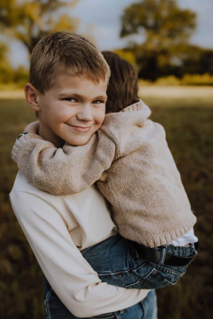 How to Prepare Your Kids for a Family Photo Session (Without the Pressure) 7 Sibling holding younger child during a relaxed family photo session outdoors
