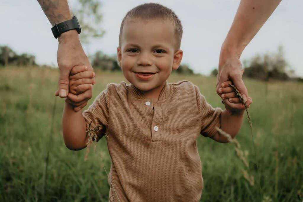 How Much Does a Family Photographer Cost in Macon GA? 8 Young boy holding his parents’ hands during a candid outdoor family session