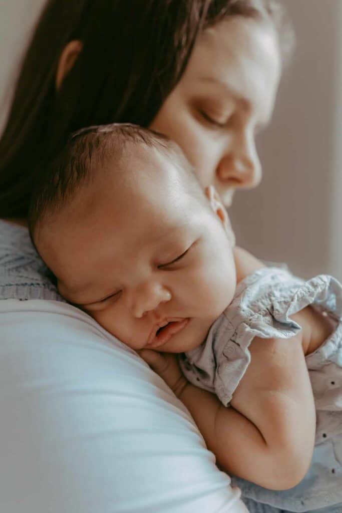 Do Newborn Photos Have to Happen in the First Two Weeks? 9 Sleeping newborn girl resting on her mother’s shoulder during a baby-led session.