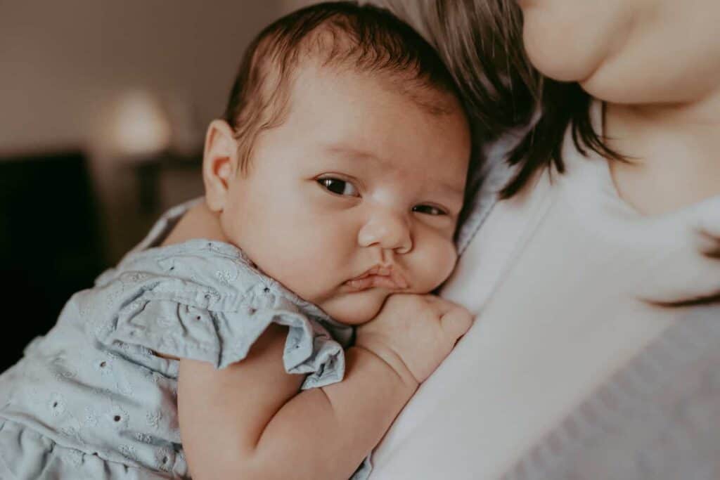 Do Newborn Photos Have to Happen in the First Two Weeks? 2 Awake baby girl resting against her mother during newborn photos after two weeks.