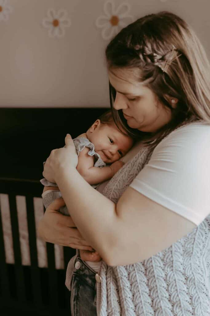 Do Newborn Photos Have to Happen in the First Two Weeks? 5 Mother cuddling her newborn daughter beside the crib during a relaxed lifestyle session.
