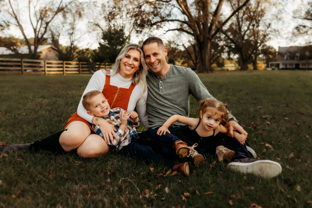 How Long Does a Family Photo Session Take? 2 Parents sitting in the grass with their two young children during an outdoor family photo session at The Wedding Barn at L'horn in Middle GA